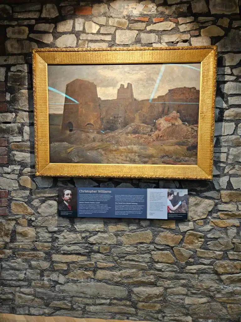 Framed painting and interpretation panel on a stone wall at Maesteg Town Hall