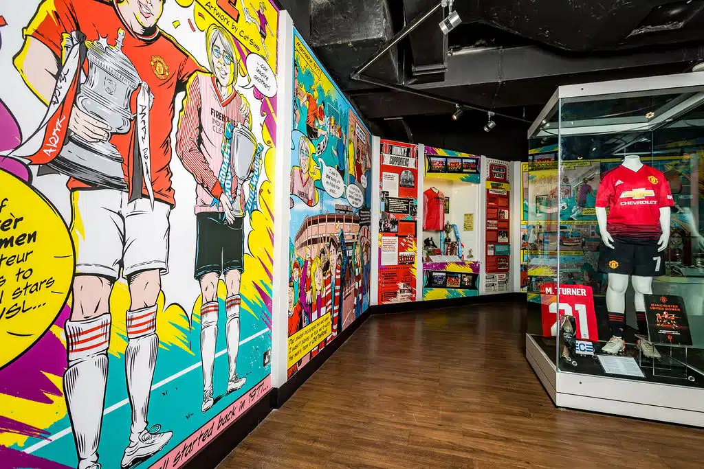 Comic-style wall graphics and display cases at the Manchester United Museum women's exhibition