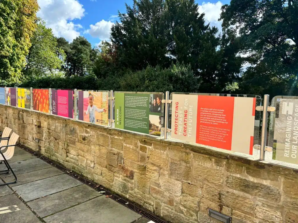 Colourful outdoor exhibition panels along a stone wall at Harewood House